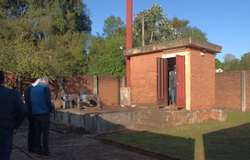 Cuatro personas de espaldas, observando un edificio de ladrillo en un entorno industrial con maquinaria de fondo y clima soleado.