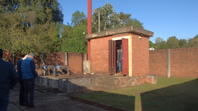 Cuatro personas de espaldas, observando un edificio de ladrillo en un entorno industrial con maquinaria de fondo y clima soleado.