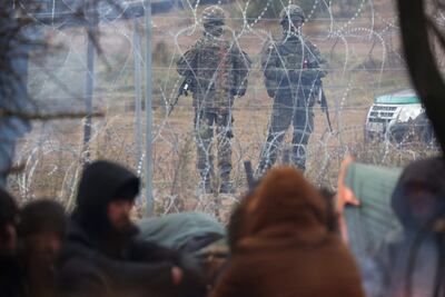 Migrantes en un campamento en la frontera entre Bielorrusia y Polonia, con soldados polacos observando desde el otro lado de la línea fronteriza, este miércoles.