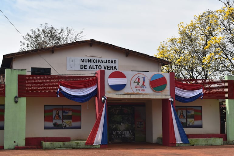 Edificio de la Municipalidad de Alto Vera decorado con banderas nacionales, cartel visible de 'MUNICIPALIDAD DE ALTO VERA'.