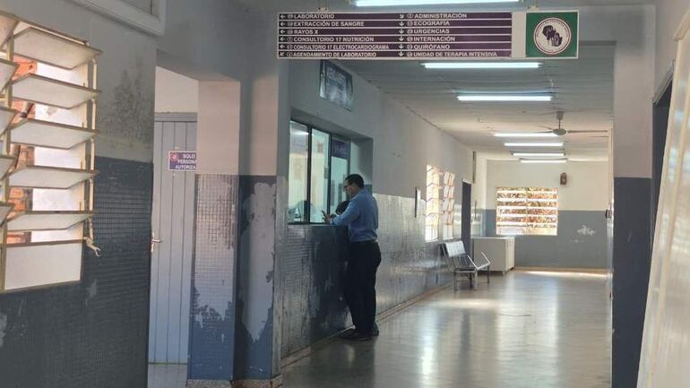 Hombre de pie frente a un mostrador con camisa azul y pantalones oscuros, en un pasillo clínico del Hospital Regional del IPS en Encarnación.