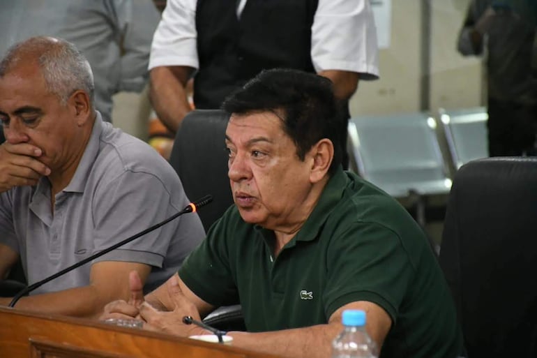 Augusto Wagner con cabello canoso, en camiseta gris, escucha mientras otro hombre de camiseta verde expone gesticulando en un salón de conferencias.
