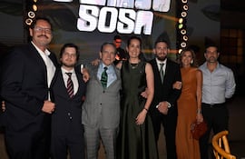 Siete personas posan felices en un evento, con vestimenta formal. Destaca un hombre de traje gris en el centro, rodeado de apoyo.