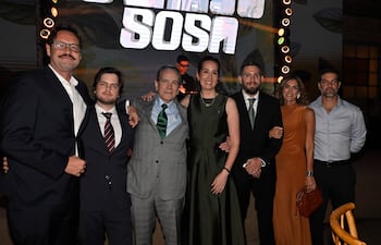 Siete personas posan felices en un evento, con vestimenta formal. Destaca un hombre de traje gris en el centro, rodeado de apoyo.