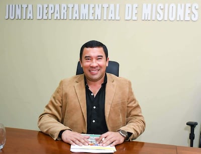 Hombre sonriente en camisa negra y saco marrón claro, sentado frente a documentos en la Junta Departamental de Misiones.