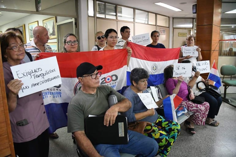 Varias personas sentadas en un banco sosteniendo pancartas y la bandera de Paraguay en un entorno de protesta.