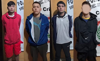 Cuatro hombres alineados frente a un cartel de Policía, con expresiones serias y vestimenta variada en un entorno institucional.