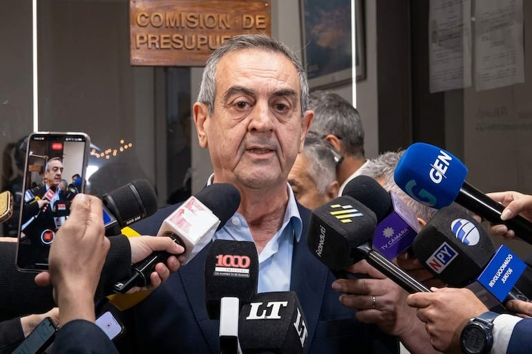 Yamil Esgaib en el centro, sosteniendo micrófonos y hablando, con múltiples cámaras enfocándolo en un entorno burocrático.