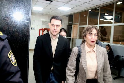 Hombre con saco negro y camisa beige conversando con mujer de atuendo a cuadros marrón en un ambiente formal.