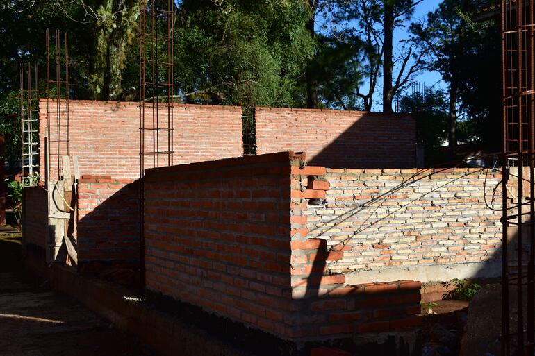 Sitio de construcción con paredes de ladrillos y estructuras de acero, rodeado de árboles y sin personas visibles.