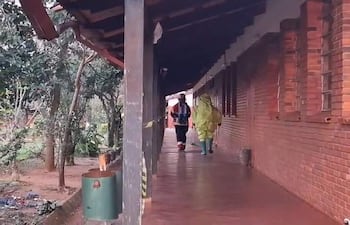 Dos bomberos, uno con traje amarillo impermeable y otro en chaqueta oscura, caminan en un pasillo de ladrillo rodeado de vegetación.