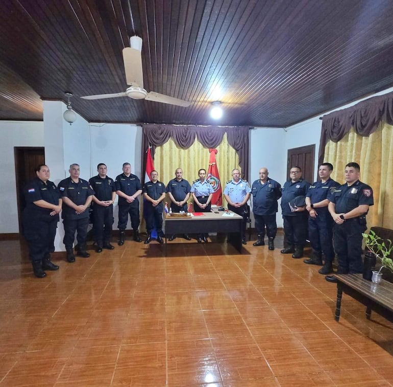 Grupo de 12 policías en uniforme, organizados en filas, escuchando atentamente durante una reunión formal en un ambiente sobrio.