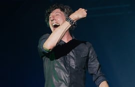 Hombre de mediana edad en camisa negra, cantando con entusiasmo en un escenario oscuro durante el concierto del Cuarteto de Nos.