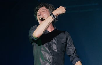 Hombre de mediana edad en camisa negra, cantando con entusiasmo en un escenario oscuro durante el concierto del Cuarteto de Nos.