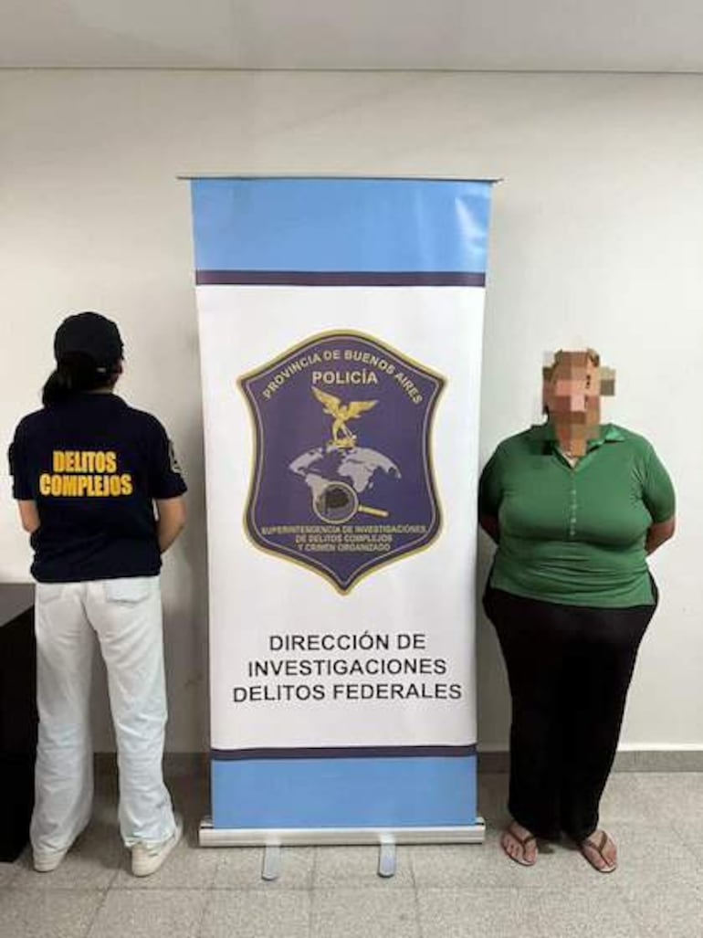 Dos mujeres en rueda de prensa; una con camiseta negra de 'Delitos Complejos' y otra en polo verde, posando en entorno oficial.