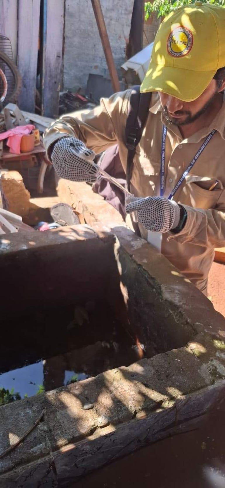 Técnico de Senepa inspecciona un recipiente con agua en un espacio abierto.