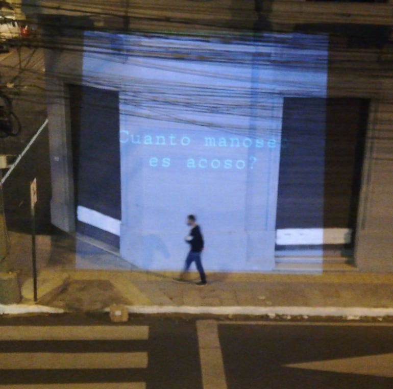 Un hombre camina junto a la pregunta "¿Cuánto manoseo es acoso?", proyectada sobre una fachada sobre la calle 25 de Mayo. Se refiere a la absolución del sacerdote católico Silvestre Olmedo, que según la Justicia corroboró, manoseó a una joven, pero aún así no fue condenado.