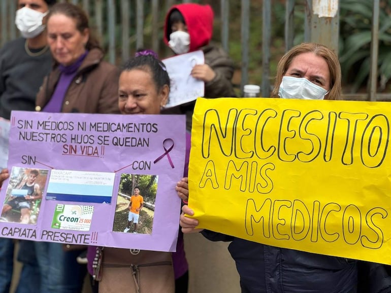 Manifestantes sosteniendo carteles, una mujer al frente sostiene cartel amarillo, ambiente urbano nublado y fresco.