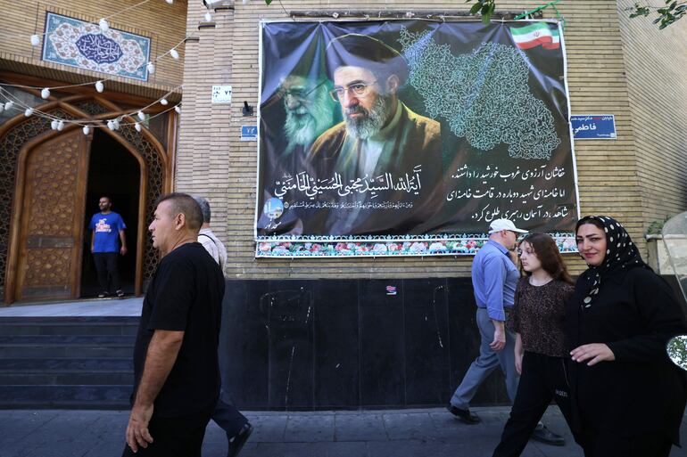 Iraníes caminan por un avenida de la capital Teherán, junto a una gigantografía del ayatolá Mojtaba Khamenei.