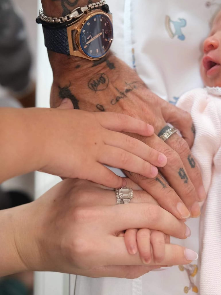 Manos entrelazadas: un adulto tatuado, una mujer y un niño en un entorno doméstico, transmitiendo cercanía familiar.