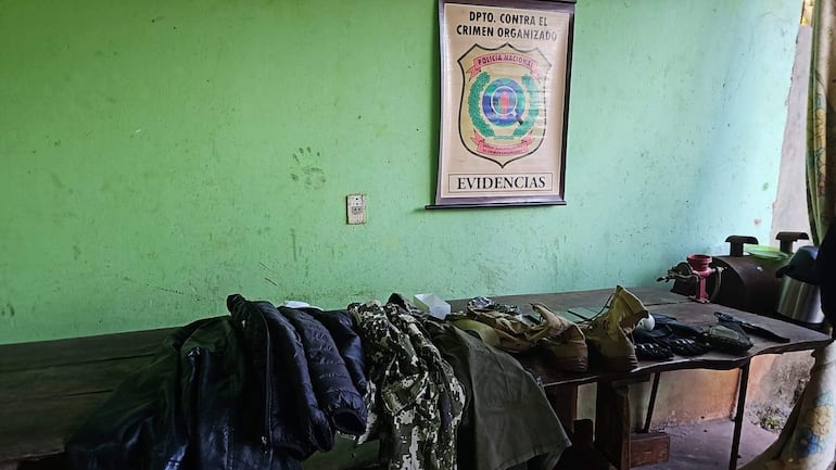 Mesa con chaquetas y botas en ambiente policial decorado con paredes verdes y cartel del Dpto. contra el crimen organizado.
