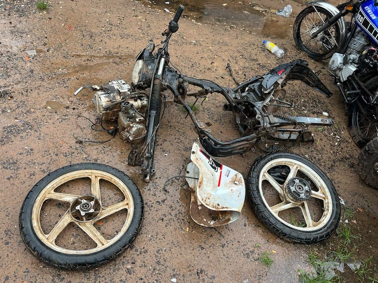 Moto desarmada en terreno de tierra con motor visible y residuos alrededor, sin personas presentes.
