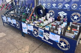 Mesa con productos confiscados, incluyendo armas y medicamentos, mientras un agente aduanero observa la escena.