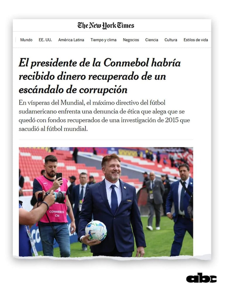 Alejandro Domínguez sonriente en traje oscuro sostiene un balón, rodeado de personas con cámaras en un ambiente de celebración deportiva.