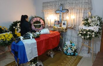 Mujer de espaldas ante altar decorado con flores y retrato del suboficial Atilio Martínez Barrios, reflejando luto y respeto.