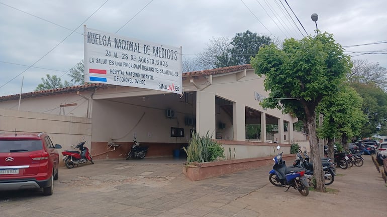 Cartel en la entrada del hospital con mensaje de huelga nacional de médicos y vehículos estacionados en un entorno urbano.