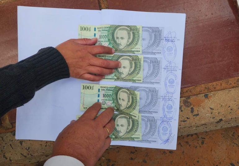 Manos sosteniendo billetes de 100 mil guaraníes sobre una superficie rígida con logotipo del Banco Central.