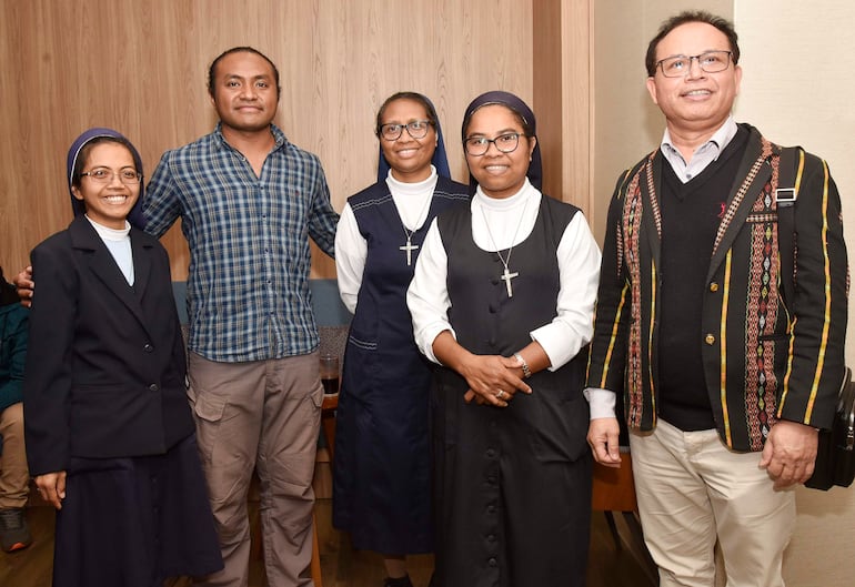 Mujeres en hábitos religiosos y hombres vestidos formalmente sonríen en un ambiente de celebración, destacando crucifijos y blazers.