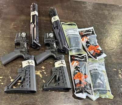 Tres rifles tipo AR-15 en posición horizontal y vertical, sobre superficie de madera, junto a varios cargadores en bolsas plásticas.