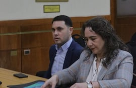 Hernán David Rivas Román en blazer oscuro observa a Alba Zaracho, quien organiza documentos en una carpeta clara a su lado.