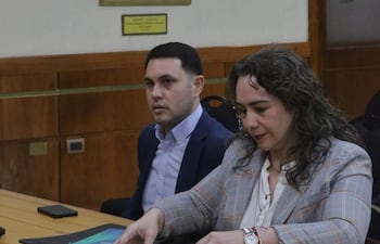 Hernán David Rivas Román en blazer oscuro observa a Alba Zaracho, quien organiza documentos en una carpeta clara a su lado.