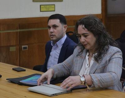 Hernán David Rivas Román en blazer oscuro observa a Alba Zaracho, quien organiza documentos en una carpeta clara a su lado.