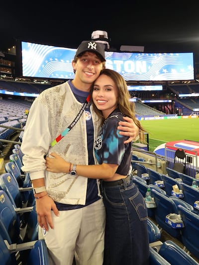 Matías Galarza sonríe abrazando a un amigo, ambos vestidos casualmente en un estadio iluminado.
