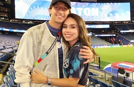 Matías Galarza sonríe abrazando a un amigo, ambos vestidos casualmente en un estadio iluminado.