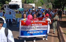 Mujeres con batas blancas sosteniendo pancartas enérgicas, rodeadas de médicos y estudiantes en una marcha colorida por la salud pública.