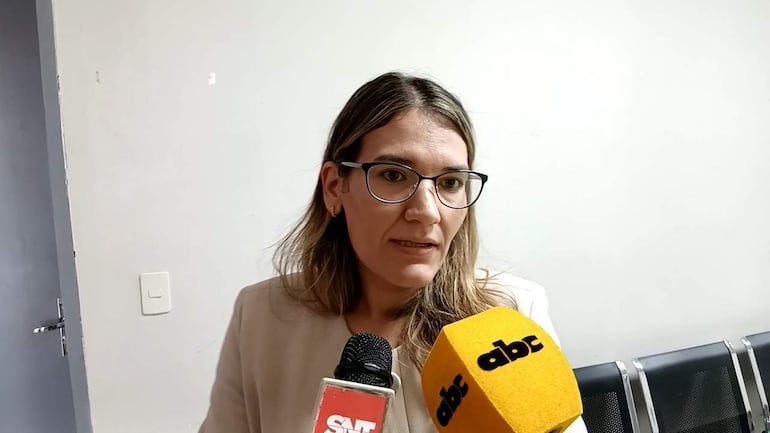 Laura Forneron, con blusa clara y gafas, habla frente a micrófonos en una sala con paredes blancas y sillas metálicas.