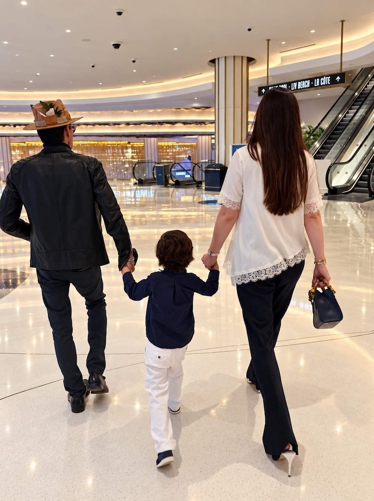 Hombre con sombrero y chaqueta de cuero camina junto a niño y mujer con blusa blanca en ambiente moderno y minimalista.