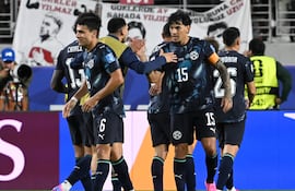 Jugadores de Paraguay en camisetas negras con escudo, uno recibe una palmada en el hombro mientras celebran juntos en el campo.