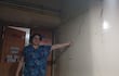 Mujer con blusa azul señala grieta en la pared, en un pasillo con letreros de acceso restringido.