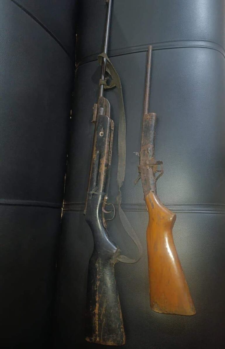 Dos rifles de diferentes tamaños apoyados sobre una superficie oscura, mostrando desgaste visible y características físicas notables.