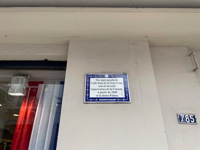 Placa en la pared de un edificio con texto sobre la historia de la Calle Real de la Vera Cruz.