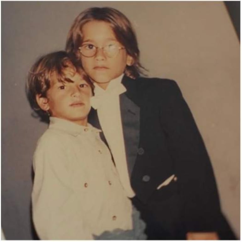 Mau y Ricky, niños, posan vestidos con chaquetas modernas y expresiones neutrales en fondo neutro.