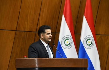 Carlos Núñez Salinas, en traje y corbata, habla desde un estrado con banderas paraguayas al fondo en un ambiente formal.