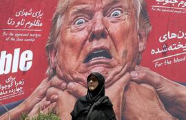 Una mujer pasa junto a una valla publicitaria antiestadounidense y anti-Trump en una calle de Teherán, Irán.
