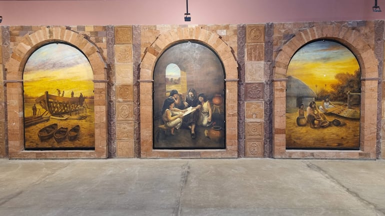 Cuatro personas en un mural, un hombre mayor enseña a mujeres, rodeados de escenas de trabajo y tradición cultural.