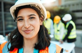 Mujer orgullosa con un casco y chaleco en una obra en construcción